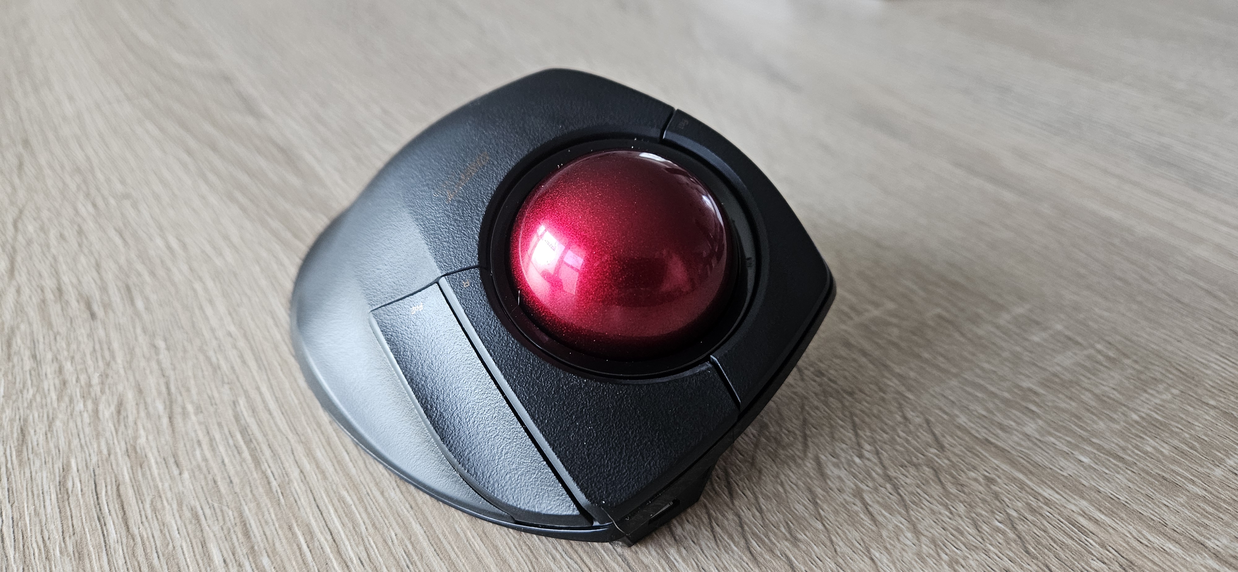 Front view of the Deft Pro (black trackball with red ball), from left to right around the ball: 1 cutom button, right click, 1 custom button