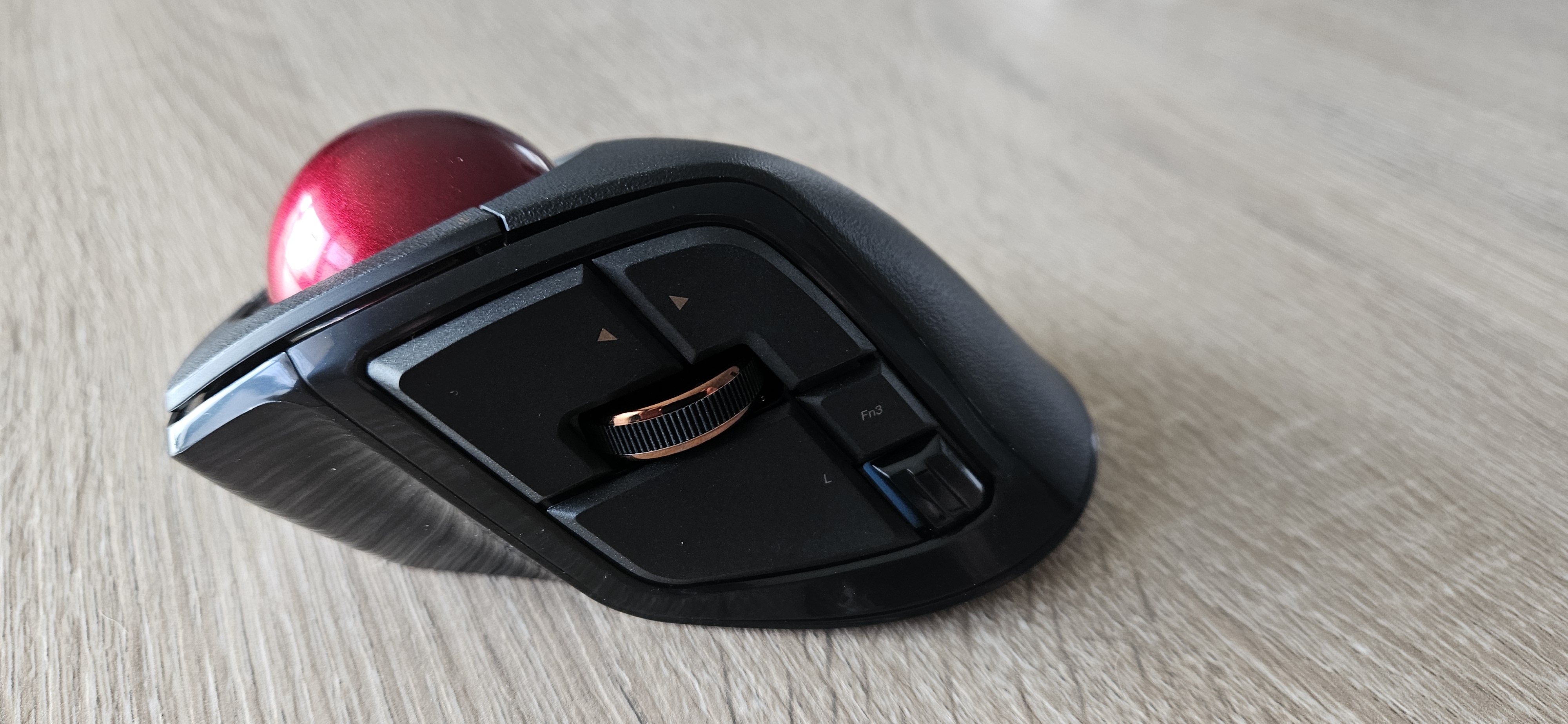 Left view of the Deft Pro (black trackball with red ball), forward and back buttons above the scroll, left click and back button below the scrol, 1 bluetooth switch button below